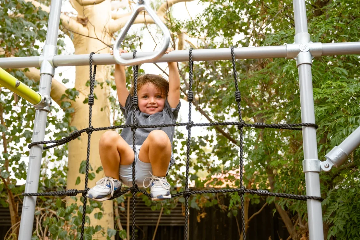 Kids using monkey bars, basketball hoop, gymnastics equipment and cubby house in a sunny Australian backyard